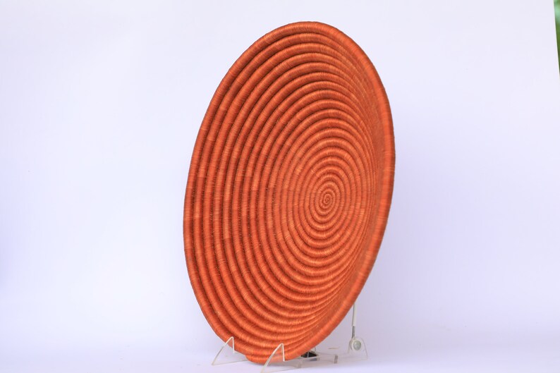 Pode incluir: Uma cesta grande, redonda e laranja tecida com um padr&atilde;o em espiral. A cesta &eacute; feita de fibras naturais e tem um aspecto r&uacute;stico e feito &agrave; m&atilde;o.