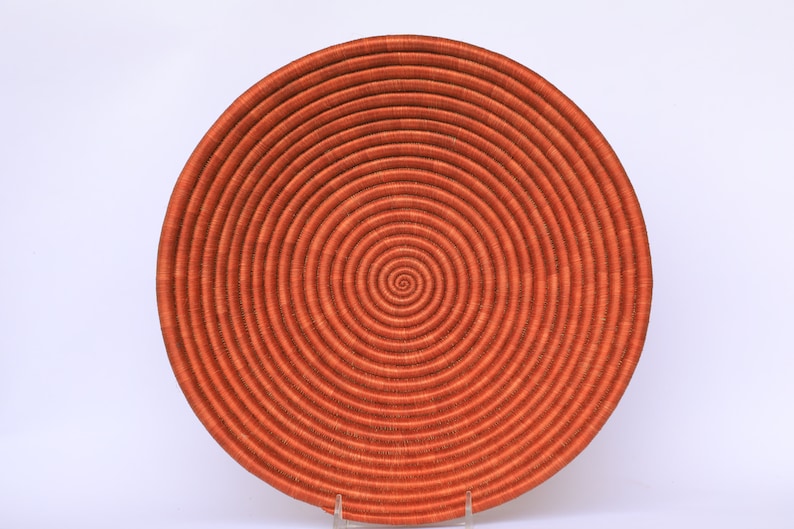 Pode incluir: Uma cesta grande, redonda e laranja tecida com um padr&atilde;o em espiral. A cesta &eacute; feita de fibras naturais e tem um acabamento liso e polido.