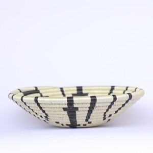 May include: A woven basket with a black and white striped pattern. The basket is round and has a shallow depth.