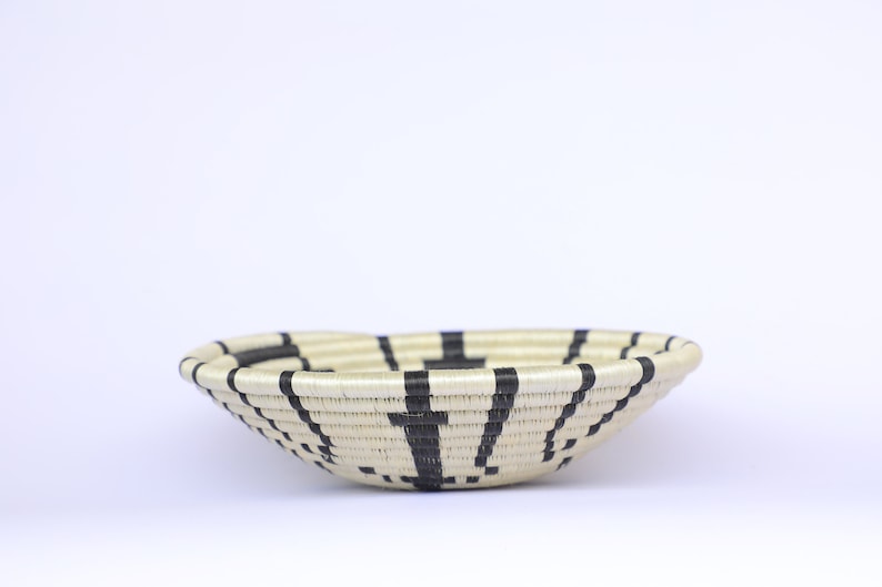 May include: A woven basket with a black and white striped pattern. The basket is round and has a shallow depth.