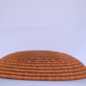 Pode incluir: Uma cesta grande, redonda e tecida feita de fibras naturais. A cesta &eacute; marrom e tem uma textura lisa e uniforme. &Eacute; perfeita para guardar objetos ou exibir objetos decorativos.