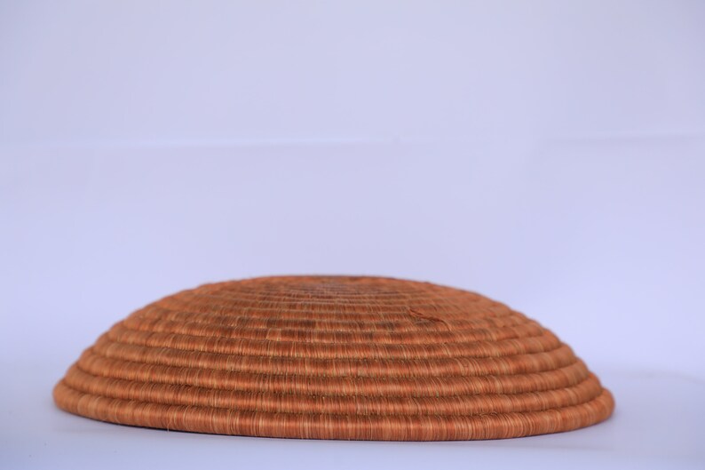 Pode incluir: Uma cesta grande, redonda e tecida feita de fibras naturais. A cesta &eacute; marrom e tem uma textura lisa e uniforme. &Eacute; perfeita para guardar objetos ou exibir objetos decorativos.