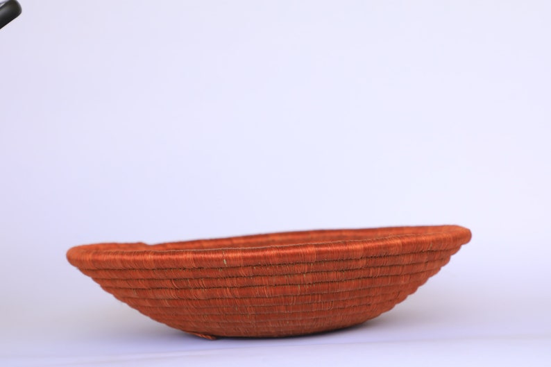 Pode incluir: Uma cesta grande, redonda e tecida feita de fibras naturais. A cesta &eacute; de cor laranja intensa e tem uma superf&iacute;cie lisa ligeiramente curva.