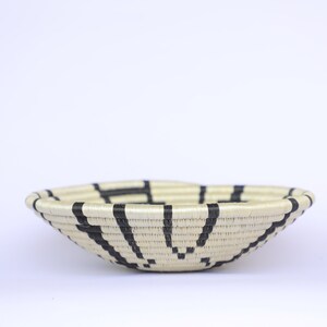 May include: A woven basket with a black and white geometric pattern. The basket is made of natural materials and has a round shape.