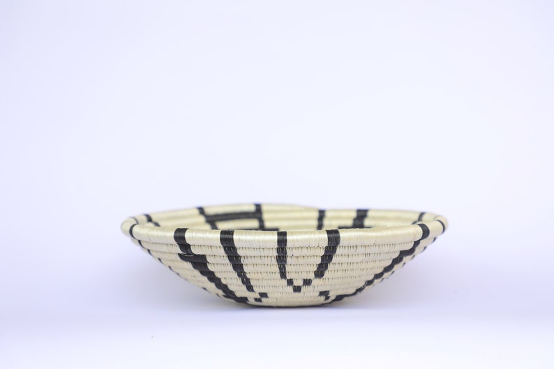 May include: A woven basket with a black and white geometric pattern. The basket is made of natural materials and has a round shape.