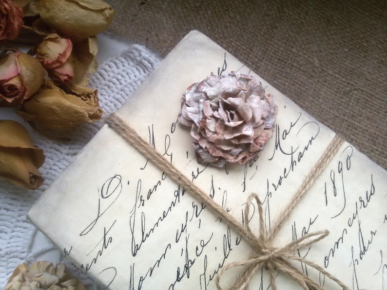 May include: A vintage-style letter tied with twine and decorated with a delicate, light brown and white paper flower. The letter is addressed to "Mr. O' France" and dated "May 1890".