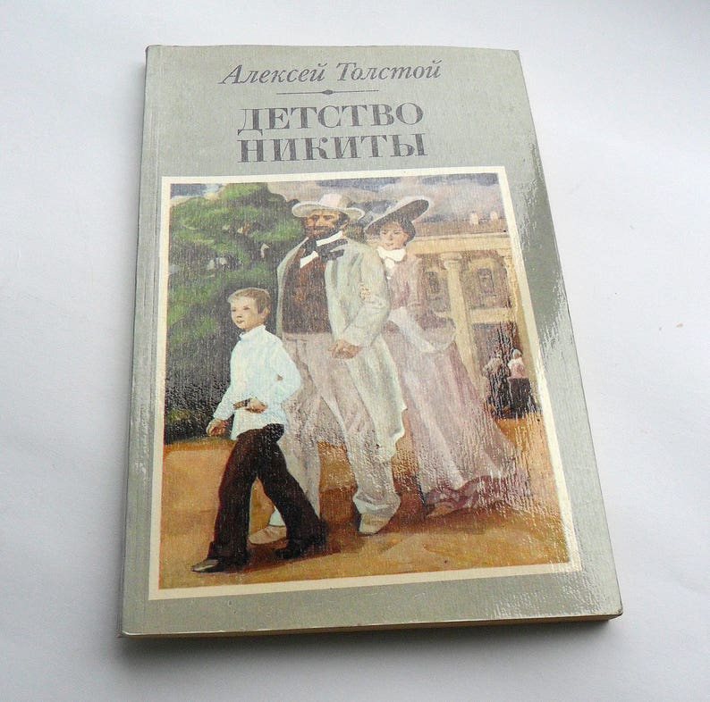 May include: A vintage paperback book cover with a painting of three people walking in a garden. The book title is "Детство Никиты" and the author is "Алексей Толстой".