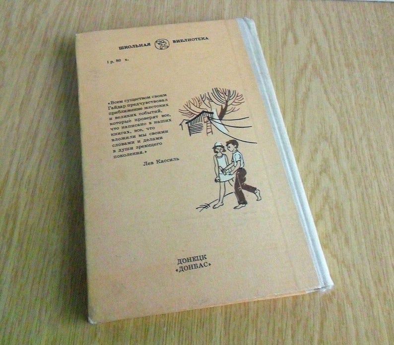 May include: A tan book with a black and white illustration of two children walking. The book's title is "ШКОЛЬНАЯ БИБЛИОТЕКА" and the author is "Лев Кассиль". The book is published by "ДОНЕЦК "ДОНБАС"".