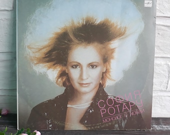Puede incluir: Una portada de disco de vinilo con una mujer con el pelo al viento. La portada es de color azul claro y gris con el texto "София Ротару Монолог о любви" en rosa.