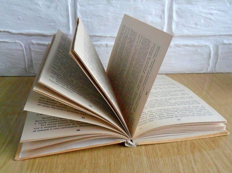 May include: An open book with pages filled with text in a foreign language. The book is lying open on a wooden surface.