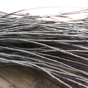 Puede incluir: Un manojo de finas ramitas grises, probablemente ramas de sauce, dispuestas en forma de cruz sobre una superficie de madera.