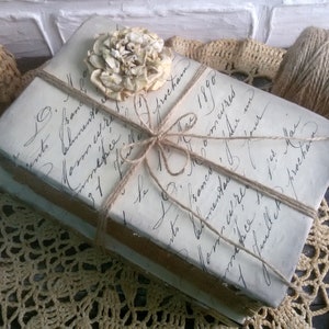May include: Two vintage books wrapped in twine and tied with a bow. A dried flower is placed on top of the books. The books are sitting on a crocheted doily.