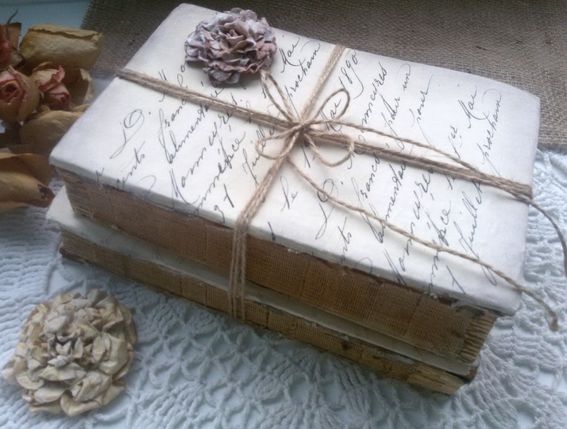 May include: Two vintage books wrapped in twine and decorated with a white flower. The books are tied with twine and have a handwritten inscription on the cover.