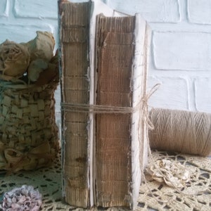 May include: Two vintage books with brown covers and white spines are tied together with twine. The books are sitting on a white crocheted doily.