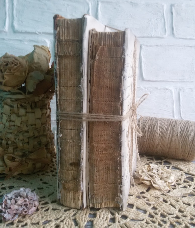 May include: Two vintage books with brown covers and white spines are tied together with twine. The books are sitting on a white crocheted doily.