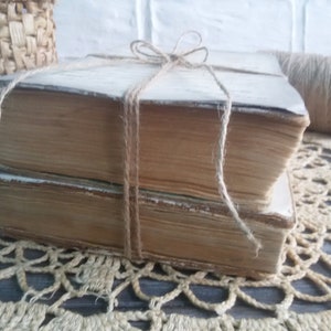 May include: Two vintage books tied together with twine, resting on a crocheted doily.
