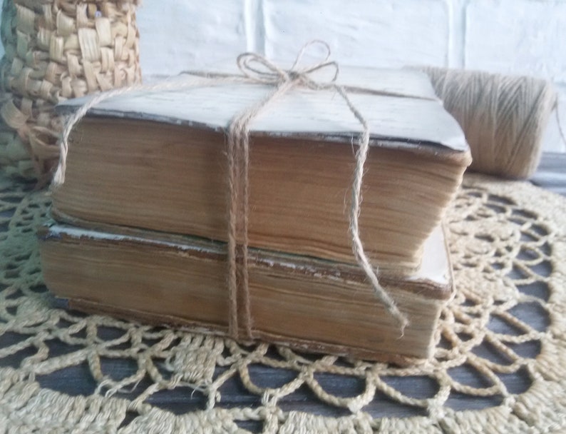 May include: Two vintage books tied together with twine, resting on a crocheted doily.