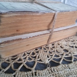 May include: Two antique books bound together with twine. The books have aged, yellowed pages and are stacked on a crocheted doily.