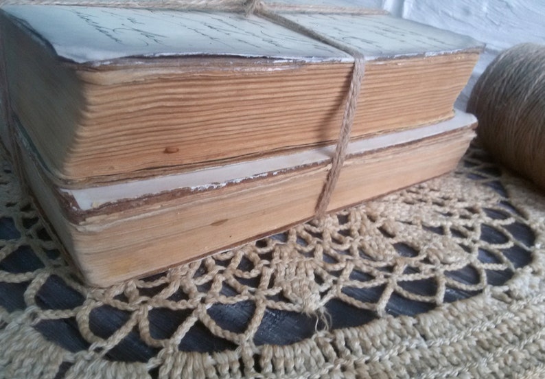 May include: Two antique books bound together with twine. The books have aged, yellowed pages and are stacked on a crocheted doily.