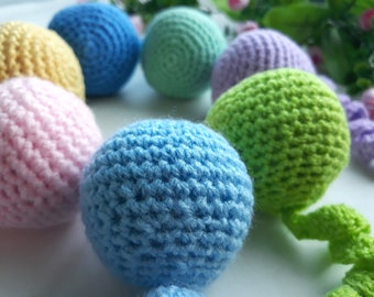 May include: A set of crocheted balls in various colors, including pink, blue, green, yellow, and purple. The balls are arranged in a circle, with the green ball in the center.