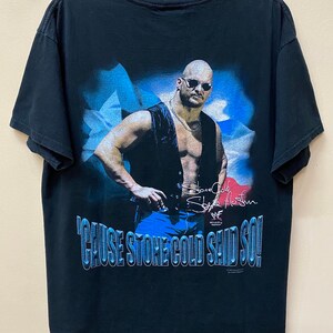 May include: Black t-shirt with a graphic of Stone Cold Steve Austin in a leather vest and sunglasses. The graphic is set against a blue and white background. The text "'Cause Stone Cold Said So!" is printed below the graphic. The shirt has a WWE logo.