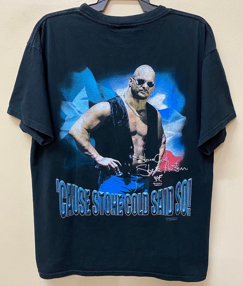 May include: Black t-shirt with a graphic of Stone Cold Steve Austin in a leather vest and sunglasses. The graphic is set against a blue and white background. The text "'Cause Stone Cold Said So!" is printed below the graphic. The shirt has a WWE logo.
