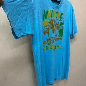 May include: A light blue t-shirt with a graphic print of a band called "Mudhoney" and the text "Girl Trouble".