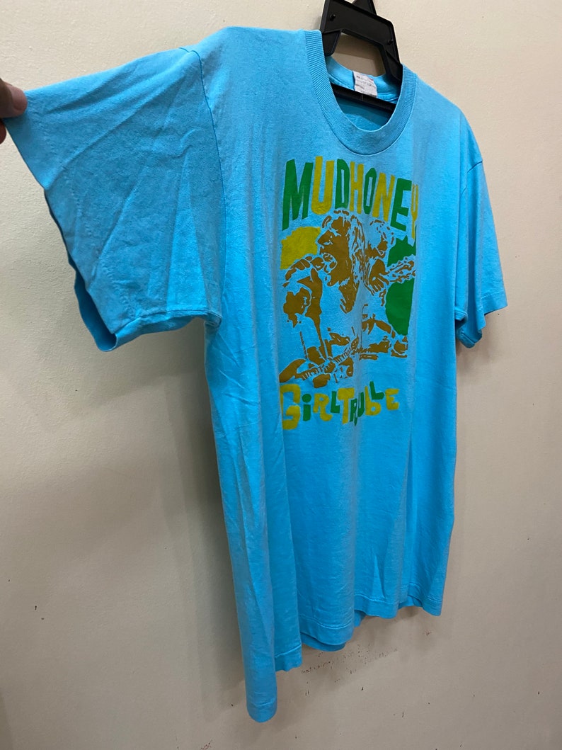 May include: A light blue t-shirt with a graphic print of a band called "Mudhoney" and the text "Girl Trouble".