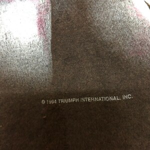 May include: A black t-shirt with white text that reads "&copy; 1994 TRIUMPH INTERNATIONAL, INC."