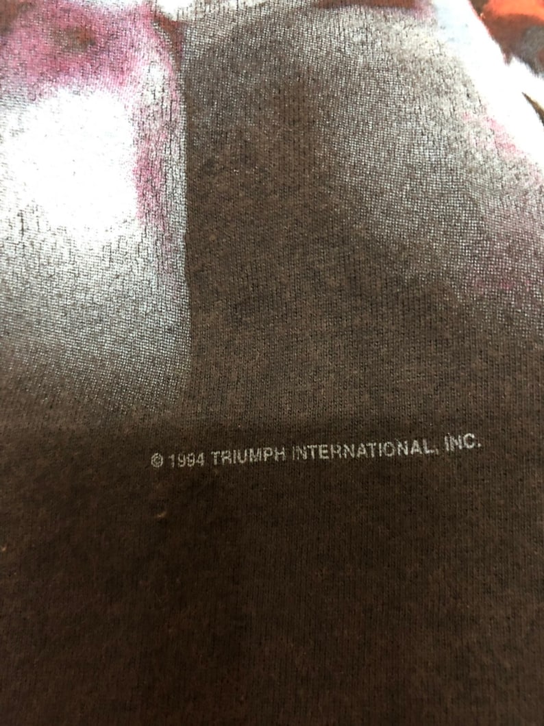 May include: A black t-shirt with white text that reads "&copy; 1994 TRIUMPH INTERNATIONAL, INC."