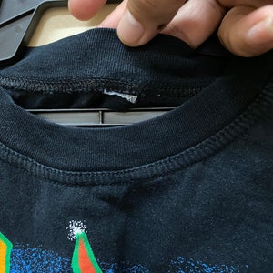 Op de afbeelding: Zwart T-shirt met een kleurrijke grafische print. De print heeft een blauw, groen, rood en geel ontwerp met een witte omtrek. Het shirt heeft een ronde hals en korte mouwen.