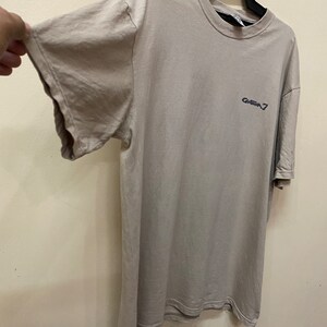 Może przedstawiać: Jasnoszary t-shirt z nadrukowanym ciemnoniebieskim logo "GHEBA 7" z przodu.