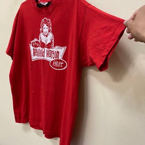 May include: Red t-shirt with a white graphic of a woman with devil horns and the text "The Rev'd Horton Heat".