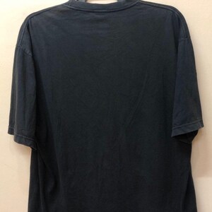 May include: Black short-sleeved t-shirt hanging on a hanger. The t-shirt is plain with no visible graphics or text.