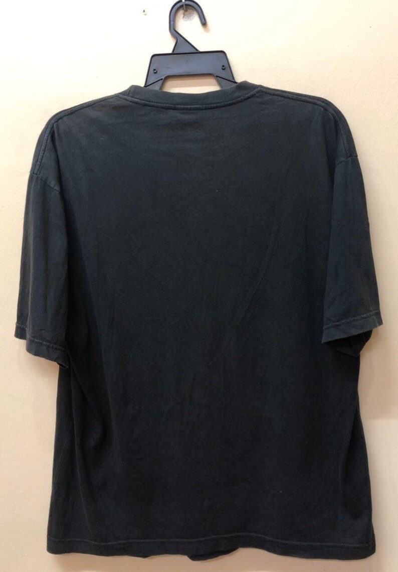 May include: Black short-sleeved t-shirt hanging on a hanger. The t-shirt is plain with no visible graphics or text.