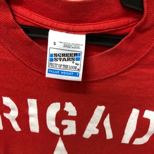 Pu&ograve; includere: Maglietta rossa con una grafica bianca di una stella e la parola "RIGAD" stampata sul davanti. La maglietta &egrave; realizzata da Fruit of the Loom ed &egrave; una maglietta Screen Stars Value Weight.