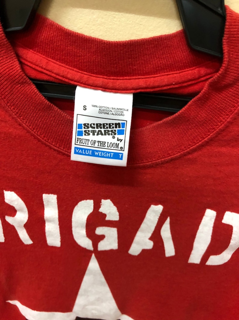 Pu&ograve; includere: Maglietta rossa con una grafica bianca di una stella e la parola "RIGAD" stampata sul davanti. La maglietta &egrave; realizzata da Fruit of the Loom ed &egrave; una maglietta Screen Stars Value Weight.