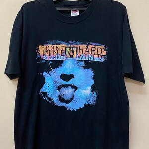 May include: Black t-shirt with a graphic print of a face with a tongue sticking out. The text "Front Line Assembly Wired" is printed on the shirt.