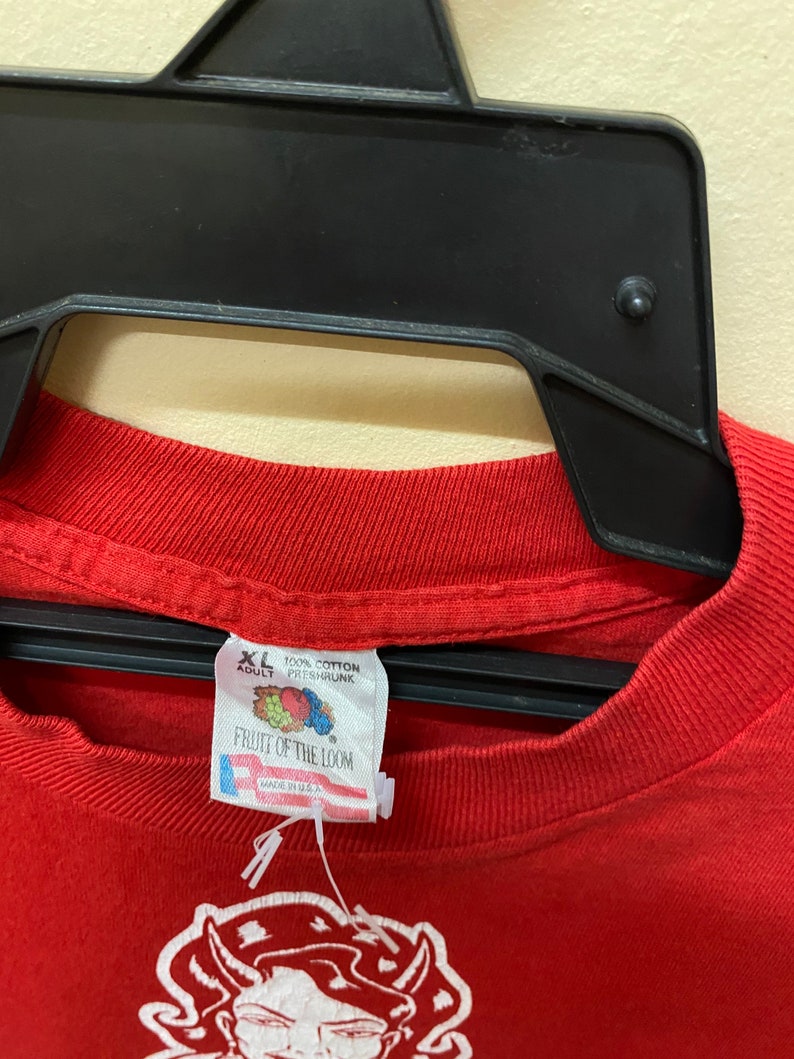 May include: Red Fruit of the Loom t-shirt with a white graphic of a cartoon devil. The tag says "XL Adult 100% Cotton Preshrunk" and "Made in U.S.A."