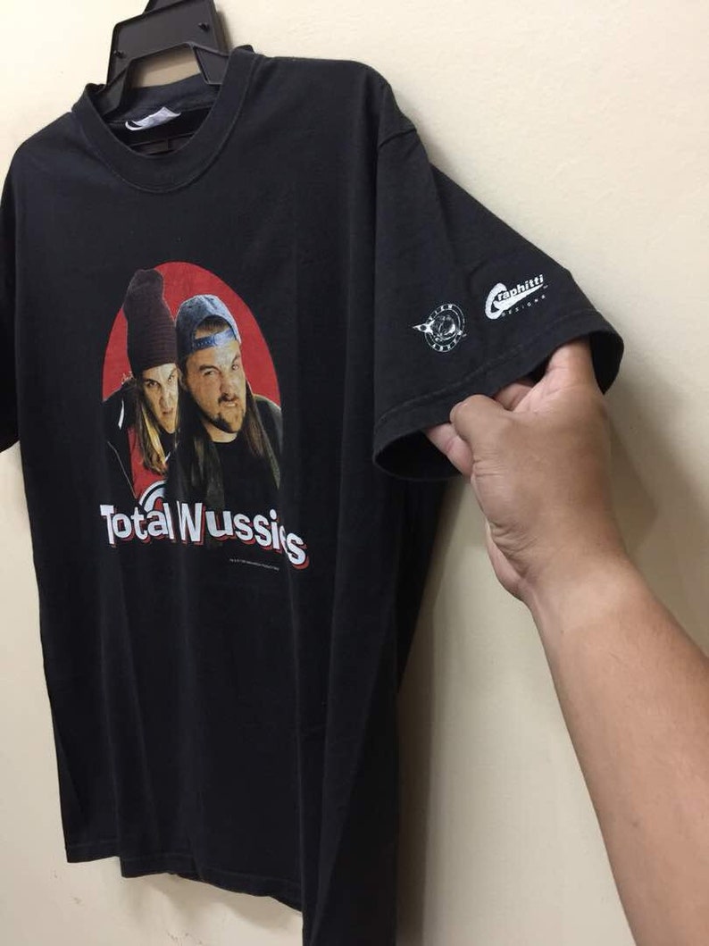 May include: Black t-shirt with a red circle graphic featuring two men with the text "Total Wussies". The t-shirt has a white "Graphiti Design" logo on the sleeve.