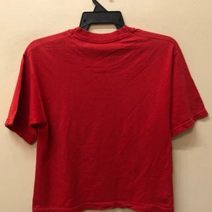 Pu&ograve; includere: Una maglietta a maniche corte di colore rosso, appesa a un'appendiabiti nero.