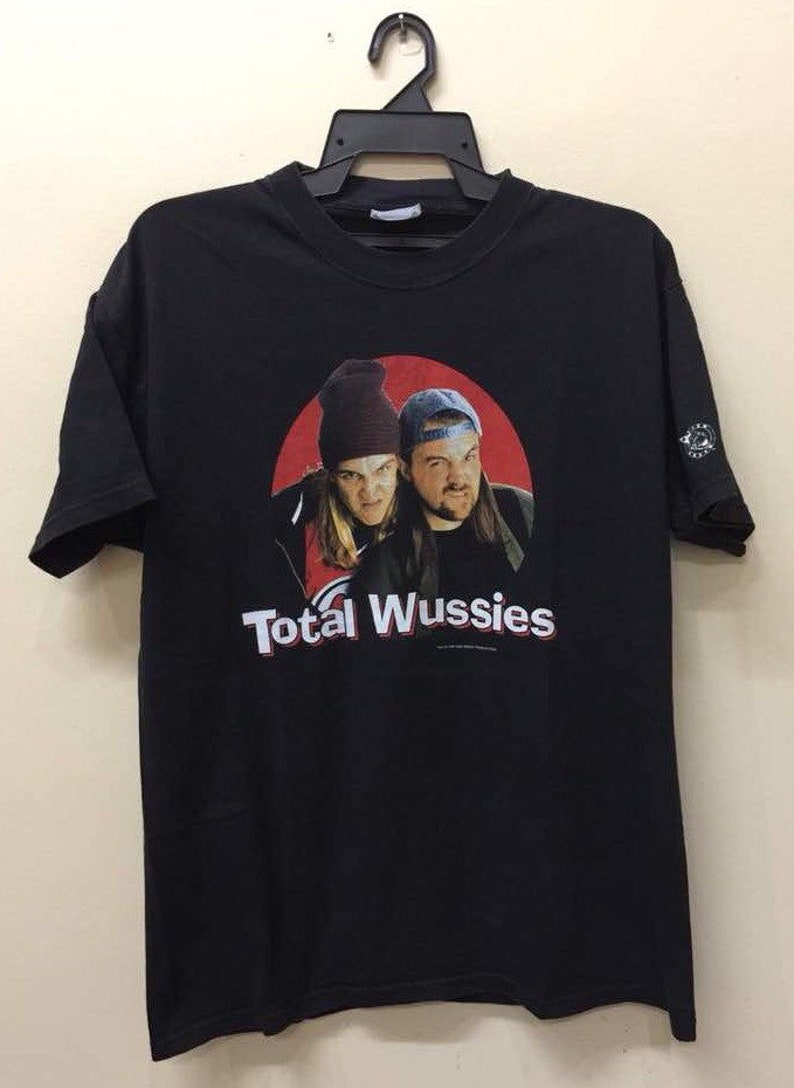 May include: Black t-shirt with a red circle graphic featuring two men with the text "Total Wussies" printed below.