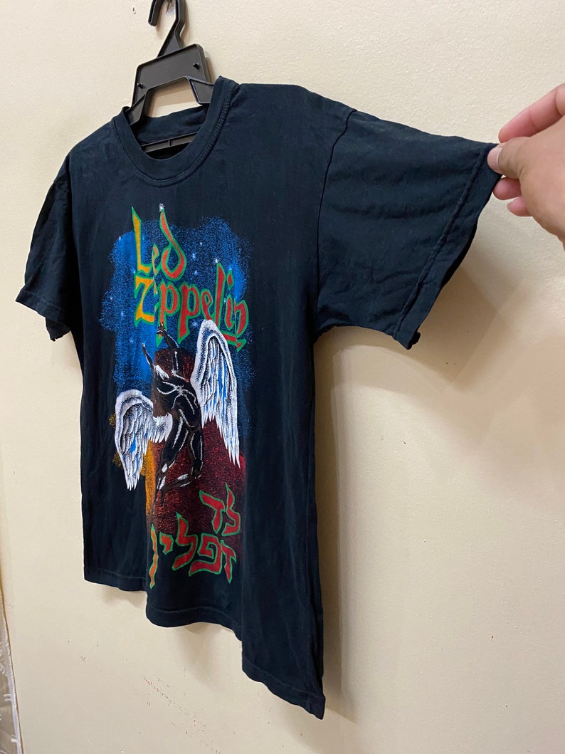 Op de afbeelding: Zwart T-shirt met een grafische print van Led Zeppelin met een engel en de bandnaam in een gestileerd lettertype. De grafiek is in tinten blauw, rood, geel en wit.