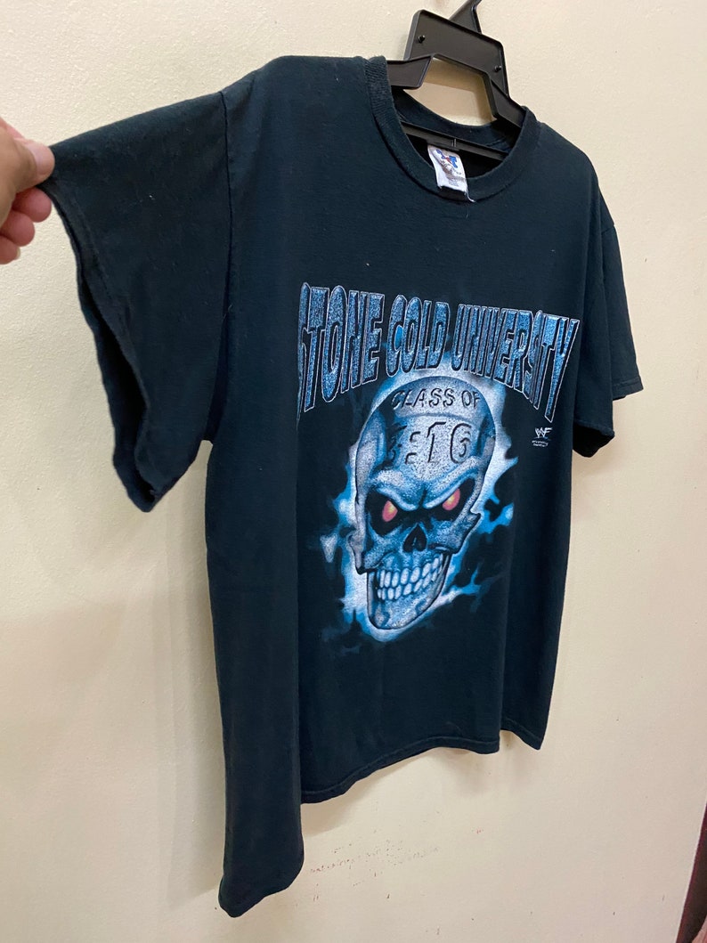 May include: Black t-shirt with a blue and white graphic of a skull with red eyes. The graphic says "Stone Cold University Class of 97" and has a WWF logo.