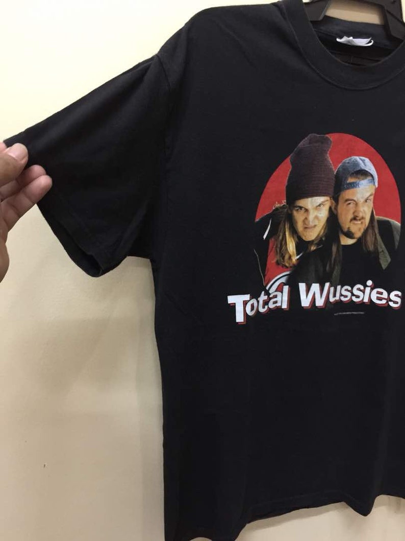 May include: Black t-shirt with a red circle graphic featuring two men wearing hats. The text "Total Wussies" is printed below the graphic.