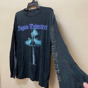May include: Black long-sleeved t-shirt with a graphic print of Yngwie Malmsteen's face and a sword. The text "Yngwie Malmsteen" is printed in purple on the front of the shirt.
