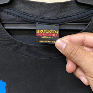May include: Black t-shirt with a blue graphic print and a Brockum Worldwide tag. The tag is red and black and says "Made in U.S.A." and "L".