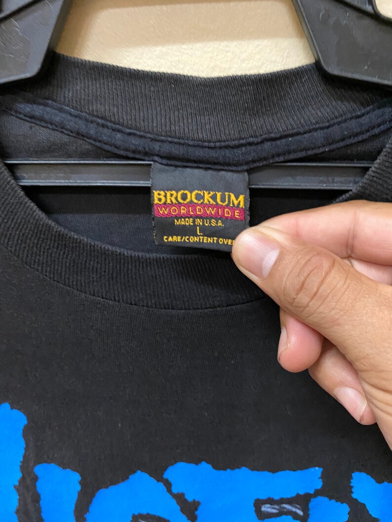 May include: Black t-shirt with a blue graphic print and a Brockum Worldwide tag. The tag is red and black and says "Made in U.S.A." and "L".