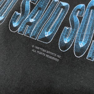 May include: Black t-shirt with a blue and white graphic that says "I Saw" with the text "&copy; 1998 TITAN SPORTS INC. ALL RIGHTS RESERVED" below.