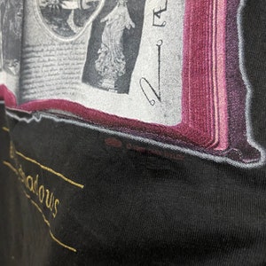 Puede incluir: Una camiseta negra con un gr&aacute;fico dorado de un libro con im&aacute;genes y el texto "The Shadows".